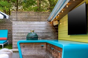 Ein Grillbereich mit Grill, einem an der Wand befestigten Fernseher und einer Sitzecke mit Stuhl und Tisch.