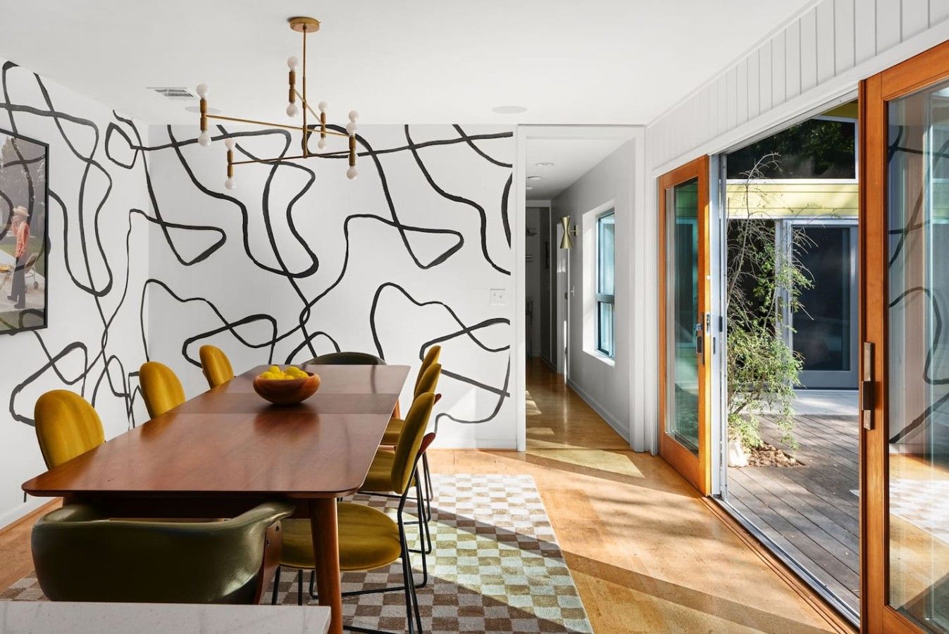 A modern dining area with a wooden table, yellow chairs, and a checkered floor.