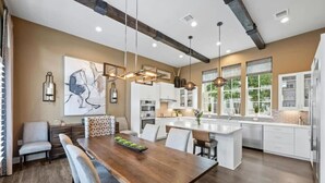 A modern kitchen with a central island, pendant lighting, and a dining area with a wooden table and chairs. - Luxe Townhome | 4bd 5ba  Elevator | 1 mile from DT (Austin)
