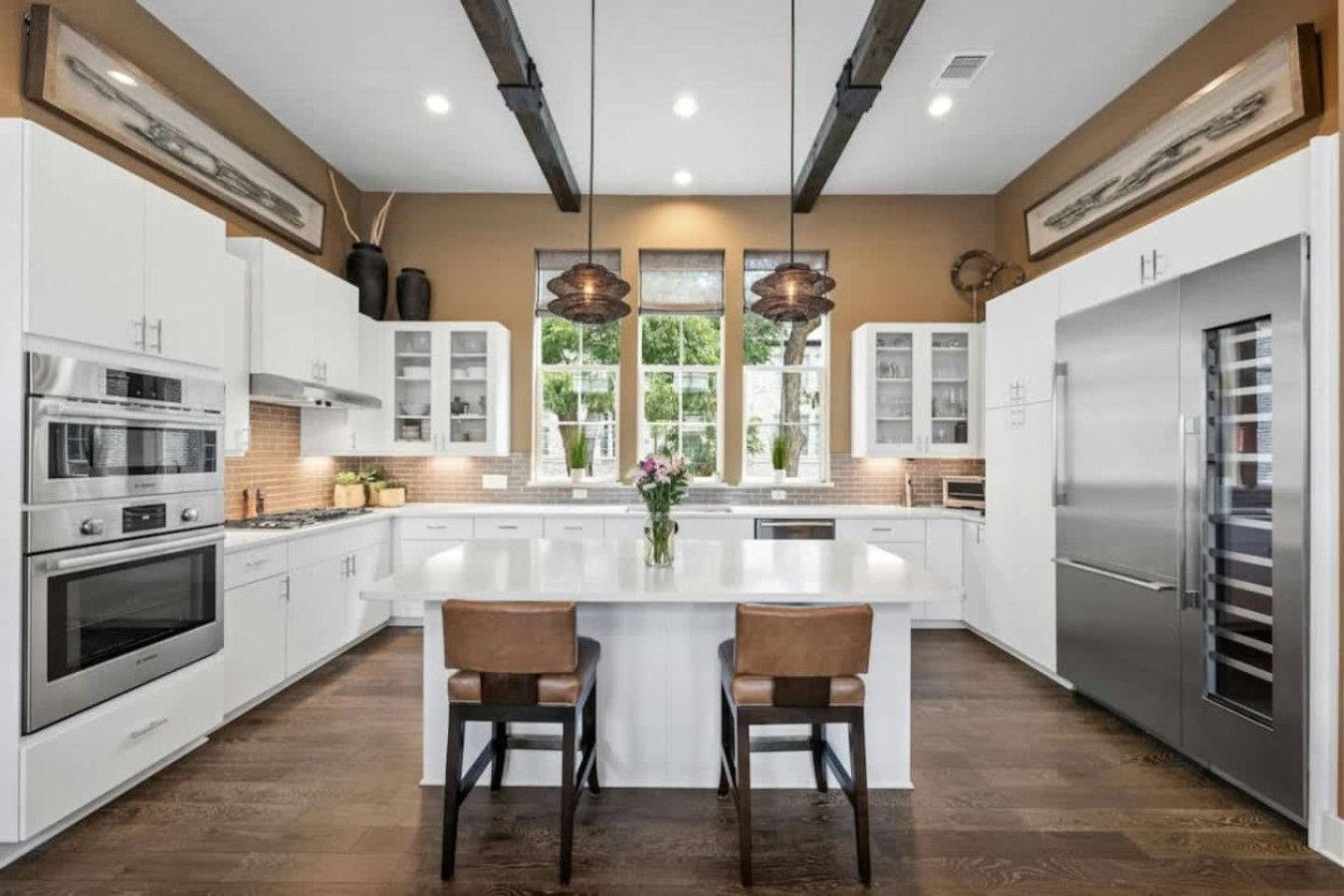 Een moderne keuken met witte kasten, roestvrijstalen apparatuur en een centraal eiland met twee barkrukken.