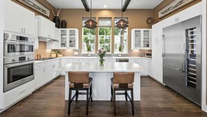 A modern kitchen with white cabinetry, stainless steel appliances, and a large island with two bar stools. - Luxe Townhome | 4bd 5ba  Elevator | 1 mile from DT (Austin)