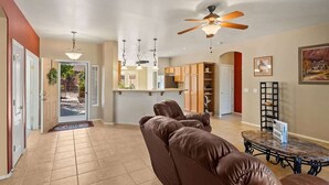A spacious living area with a brown leather sofa, a dining table, and a ceiling fan.