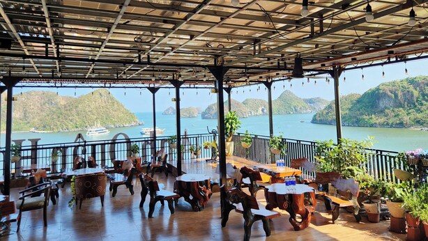 An outdoor seating area with rustic wooden furniture and a view of a lake with boats. - Anh Quân-Viewpoint Hotel (Hai Phong)