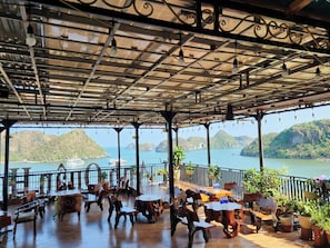 An outdoor seating area with rustic wooden furniture and a view of a lake with boats. - Anh Quân-Viewpoint Hotel (Hai Phong)