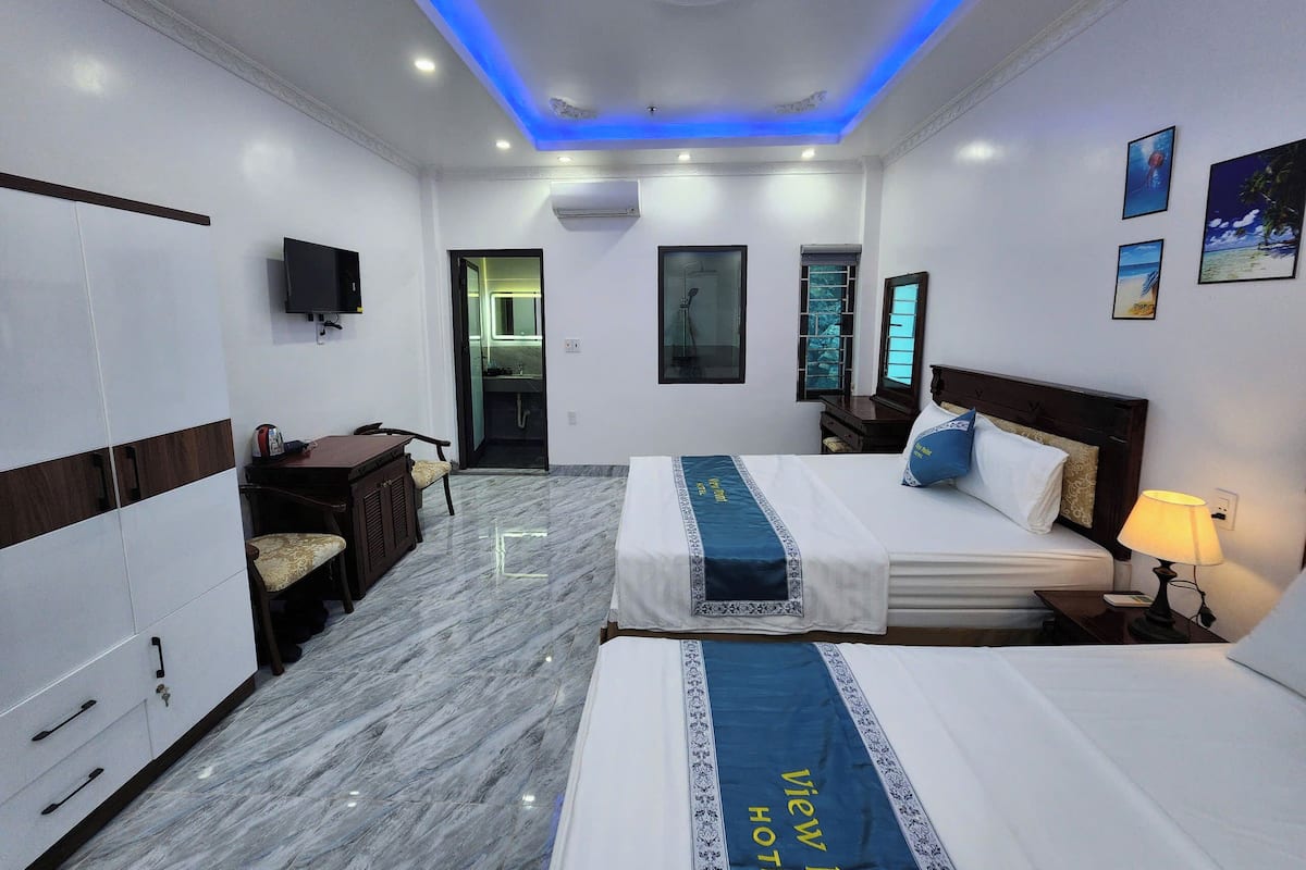 A hotel room with a bed, a desk, a wardrobe, a TV, a bathroom, and a view of the sea.