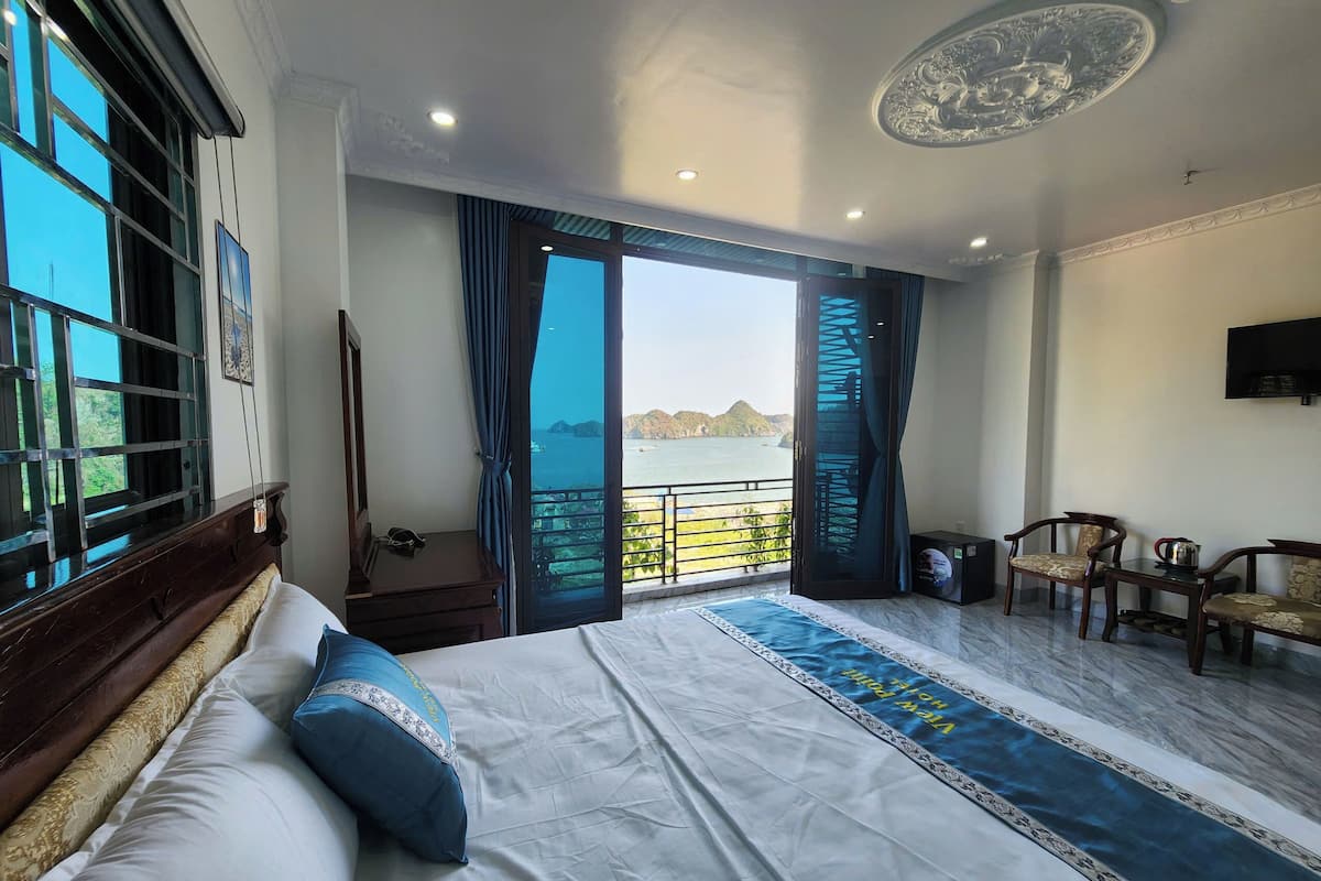 A bedroom with a large bed, a view of the sea, and a balcony with chairs.