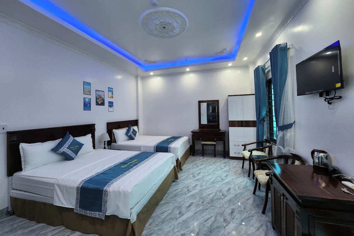 A hotel room with two beds, a desk, a chair, a TV, and a ceiling with blue lighting.