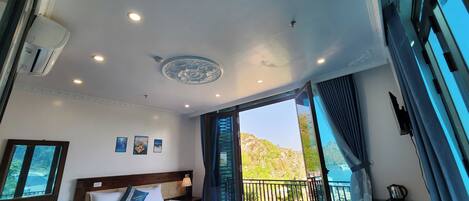 A hotel room with a large bed, a desk, and a balcony with a view of the mountains.