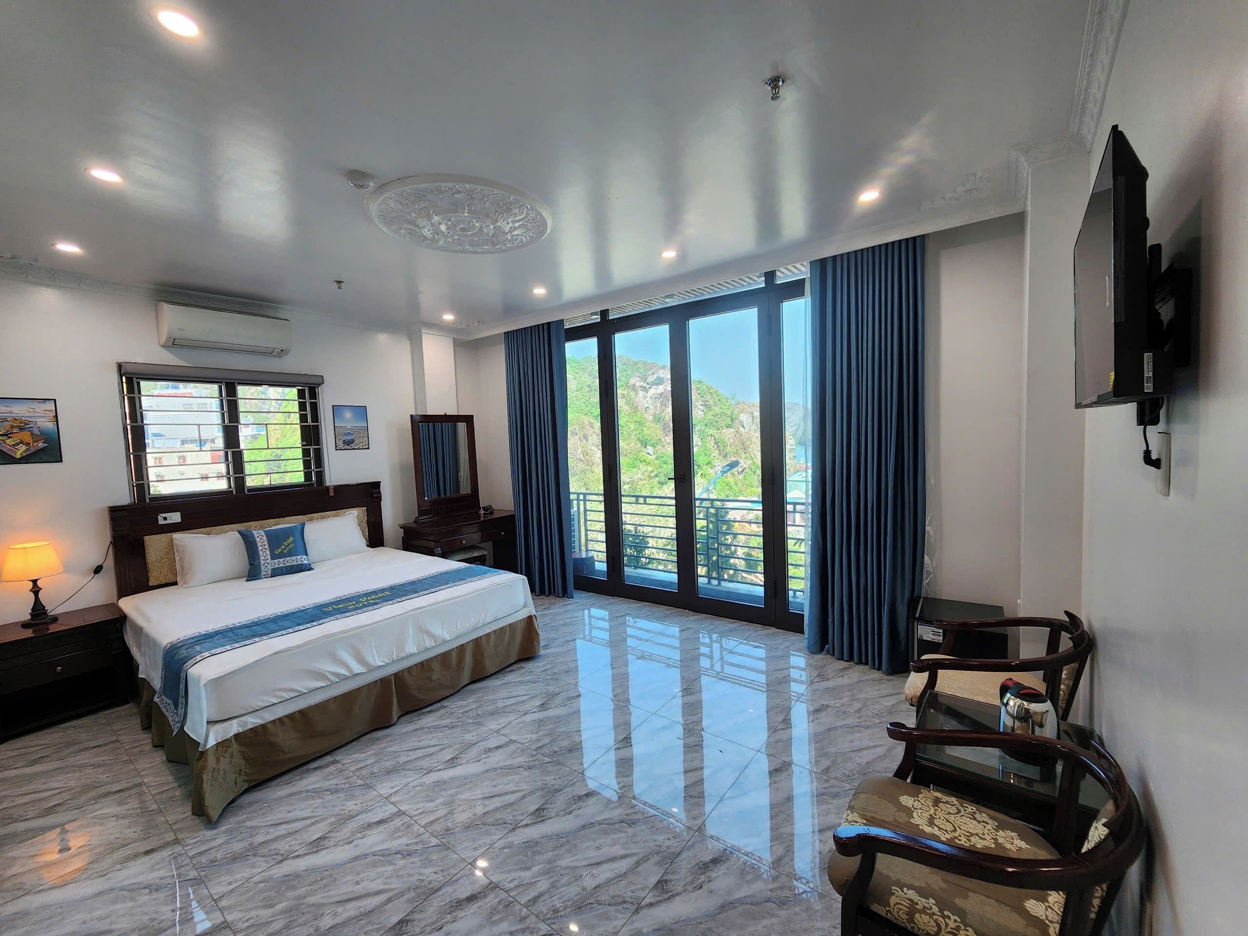Une chambre d’hôtel avec un grand lit, un bureau, une chaise, une télévision et un balcon donnant sur un espace verdoyant.