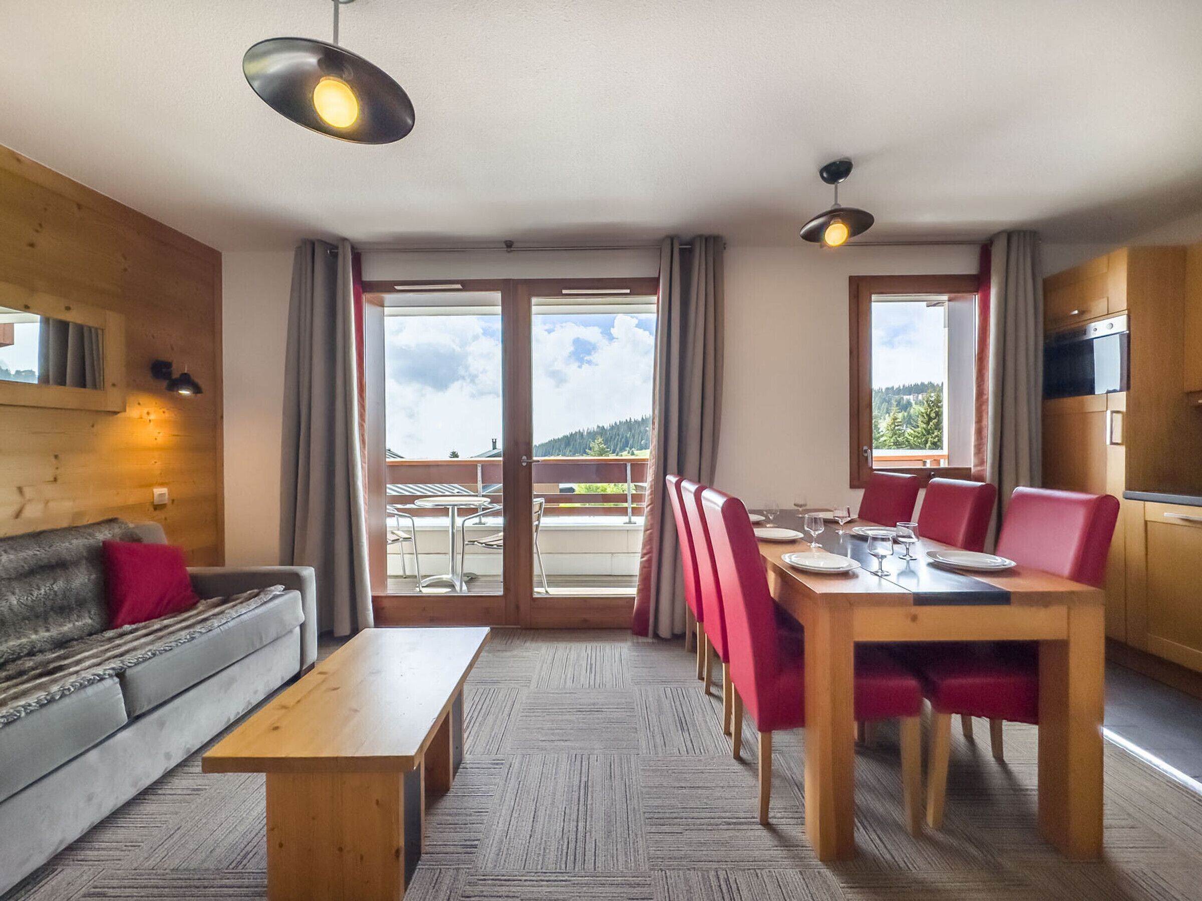 A modern hotel room with a sofa, dining table, chairs, and a balcony with a view.