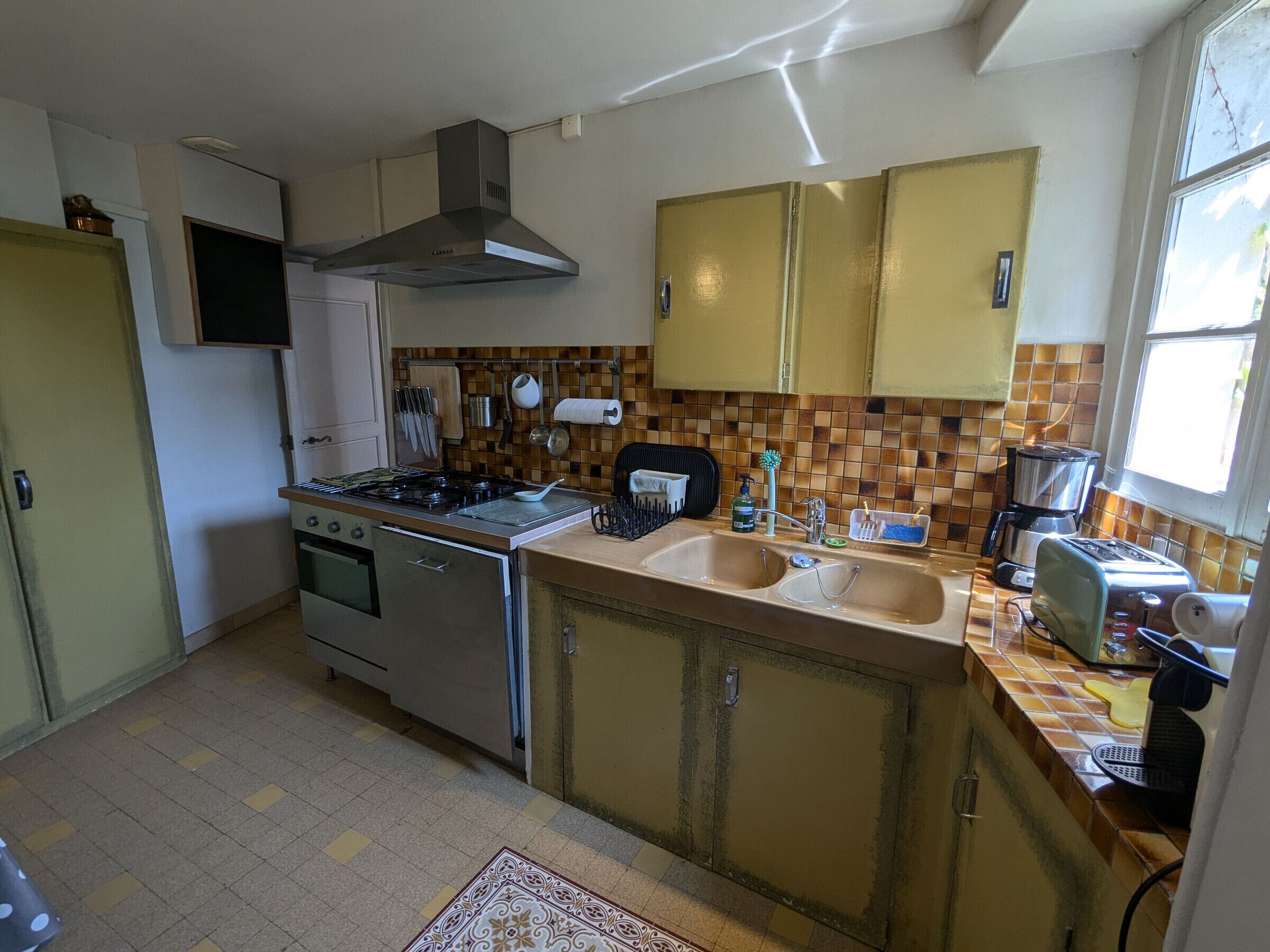 A compact kitchen with a gas stove, oven, and a sink. There are cabinets, a toaster, and a window providing natural light.