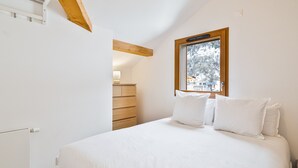 Ein Schlafzimmer mit einem Bett, einem Holzschrank, einem Fenster mit Blick auf eine verschneite Landschaft und einer Decke mit Holzbalken.