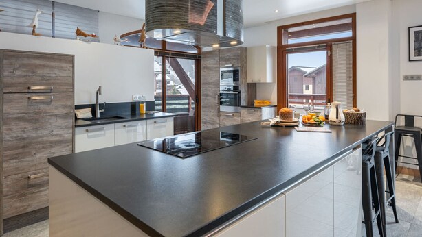 A modern kitchen with a large island, stainless steel appliances, and a view of a wooden deck. - Spacious loft with spa, pool, gym, and parking (Les Saisies)