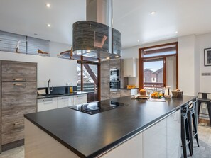 A modern kitchen with a large island, stainless steel appliances, and a view of a wooden deck. - Spacious loft with spa, pool, gym, and parking (Les Saisies)