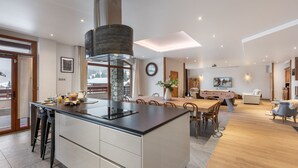 A modern kitchen with a central island, dining area with chairs, a sofa, and a TV. - Spacious loft with spa, pool, gym, and parking (Les Saisies)