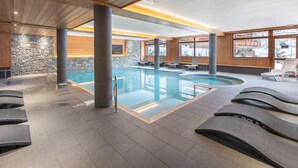 An indoor swimming pool with lounge chairs and stone walls. - Spacious loft with spa, pool, gym, and parking (Les Saisies)