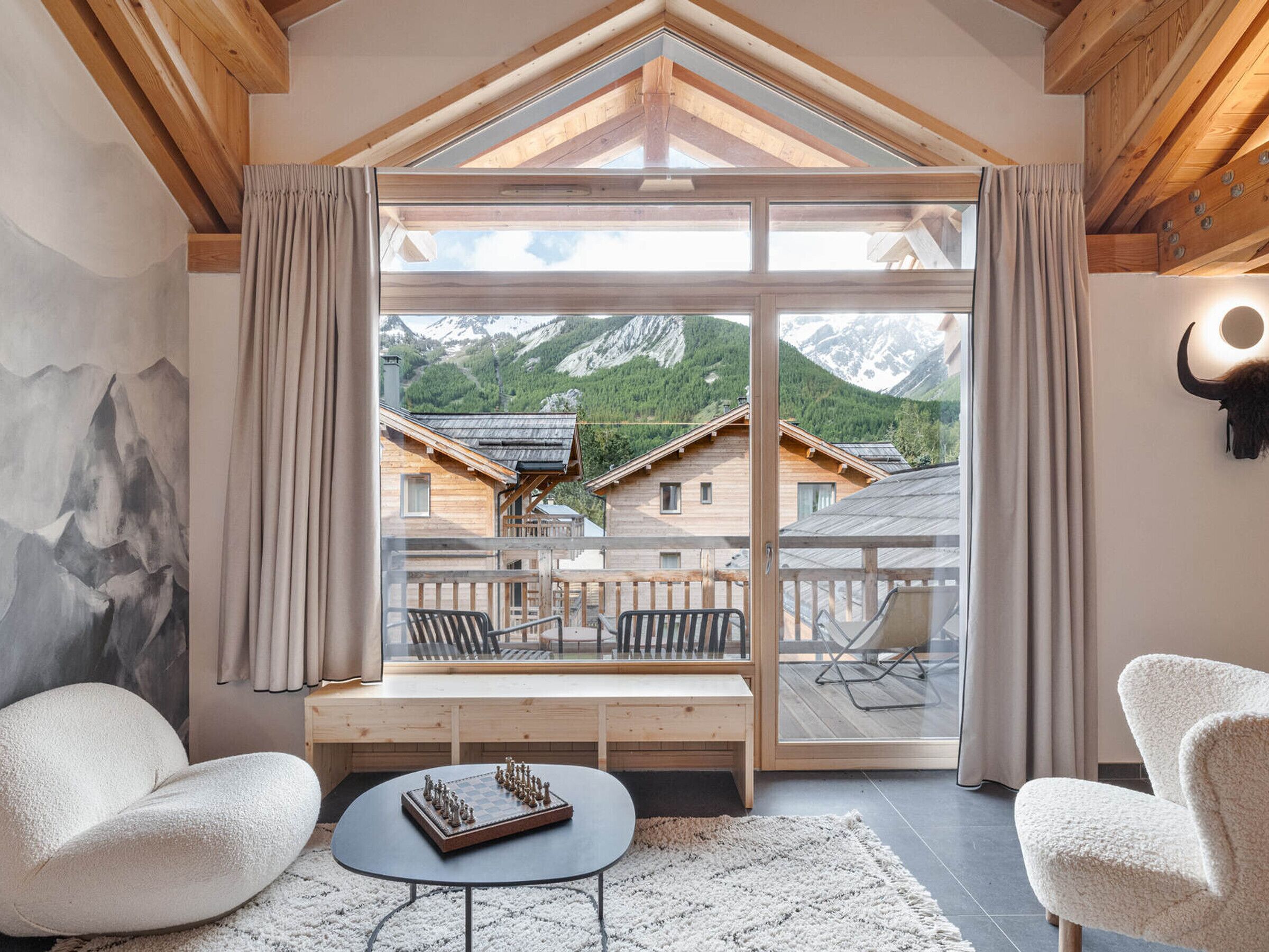 A cozy room with a large window, wooden furniture, and a chessboard.