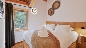 Une chambre avec un plafond en bois, un grand lit recouvert de draps blancs, une fenêtre avec des rideaux et deux assiettes décoratives accrochées au mur.