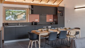 Une cuisine moderne avec des meubles de rangement sombres, une table à manger en bois et des chaises noires.