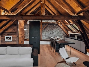 Un'accogliente soffitta rustica con travi a vista in legno, una parete in pietra, un'area pranzo con tavolo e sedie e un divano bianco.