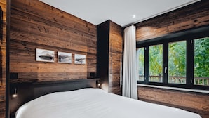 Quarto com parede de madeira, uma cama grande e janela com vista para vegetação.