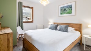 A bedroom with a wooden bed, a desk, a chair, a window with curtains, a bedside lamp, and a framed picture on the wall. - Cocooning Duplex with Terrace and Garden in Serre Chevalier (Le Monêtier-les-Bains)