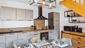 A modern kitchen with a dining area, featuring a wooden staircase, built-in cabinets, and a hanging light fixture. - Cocooning Duplex with Terrace and Garden in Serre Chevalier (Le Monêtier-les-Bains)