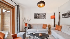 A modern living room with a grey sofa, orange armchair, and a round coffee table. There is a black pendant light, a floor lamp, and two framed pictures on the wall. - Cocooning Duplex with Terrace and Garden in Serre Chevalier (Le Monêtier-les-Bains)