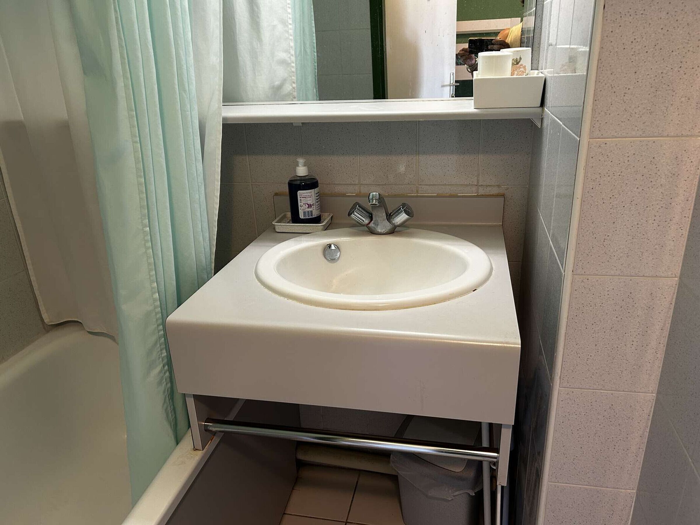 Un baño con un lavabo blanco, un espejo y un perchero para toallas.