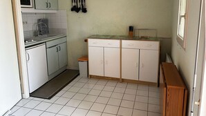 Une cuisine compacte avec des meubles blancs, un évier et un petit plan de travail. Il y a une fenêtre sur le côté droit et une porte sur le côté gauche.