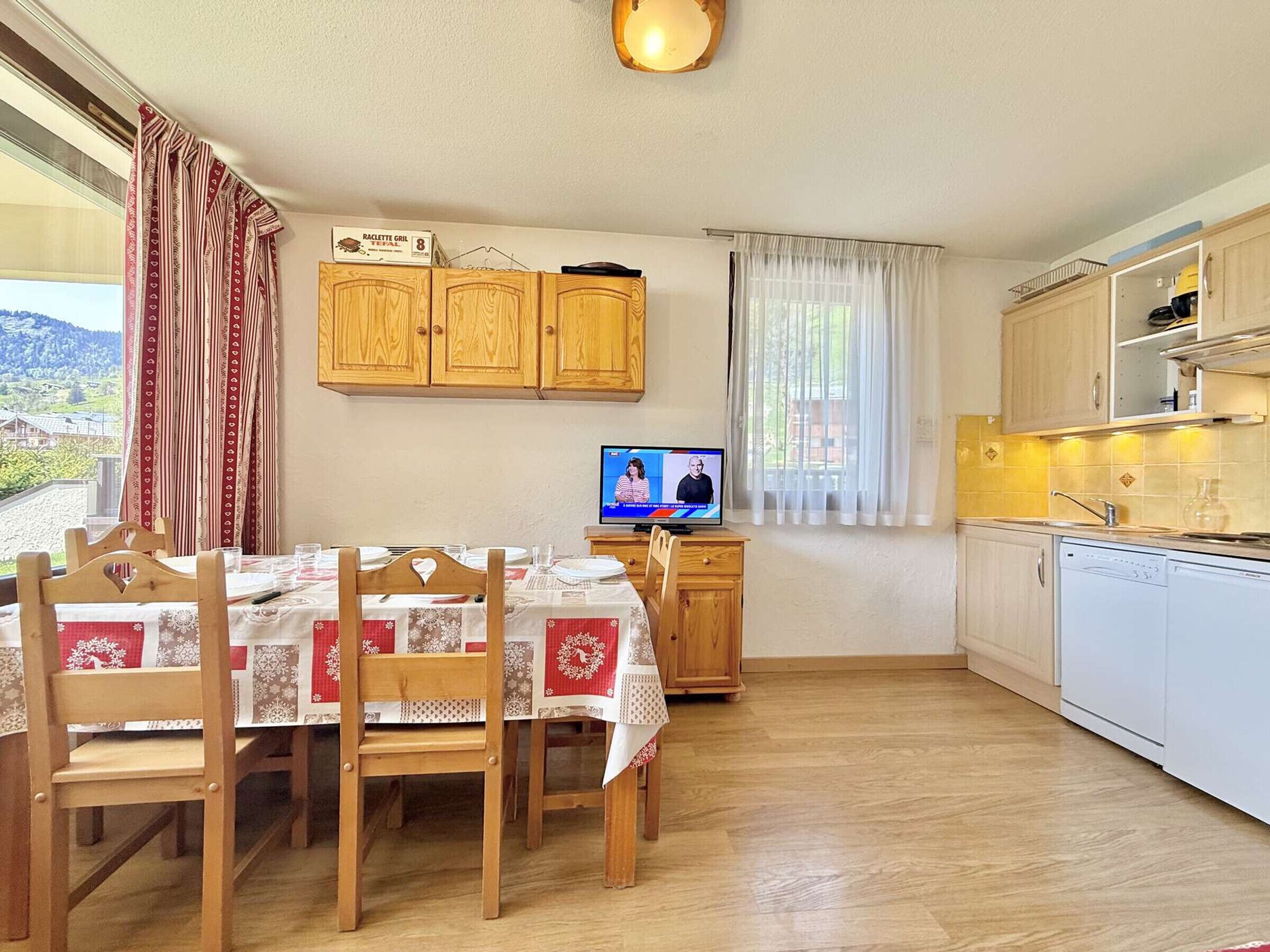Eine gemütliche Küche mit Holzausstattung, einem Esstisch für vier Personen und einem Fernseher an der Wand.