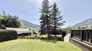 A grassy area with a wooden deck, a large coniferous tree, and a building with a metal roof.