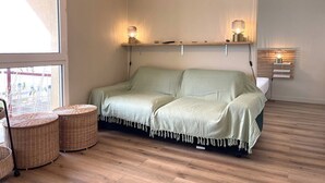 Une pièce chaleureuse avec un canapé vert, deux lampes fixées au mur, un plancher en bois et des paniers en osier.