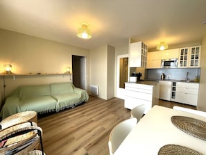 Een ruimtelijk ingerichte leefruimte met een bank, een eettafel en een kitchenette.