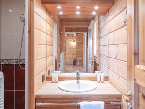 Une salle de bain rustique, avec une cabine en bois, comprenant un lavabo, un miroir et une douche.