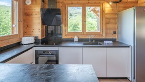 A modern kitchen with wooden walls, a stainless steel refrigerator, a built-in oven, and a window overlooking greenery. - 178m2 Chalet in Alpe d'Huez Ski-in/Ski-out with Terrace (Huez)