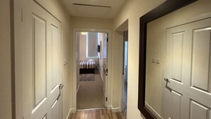 Un pasillo con piso alfombrado que conduce a un dormitorio con cama y ventana.