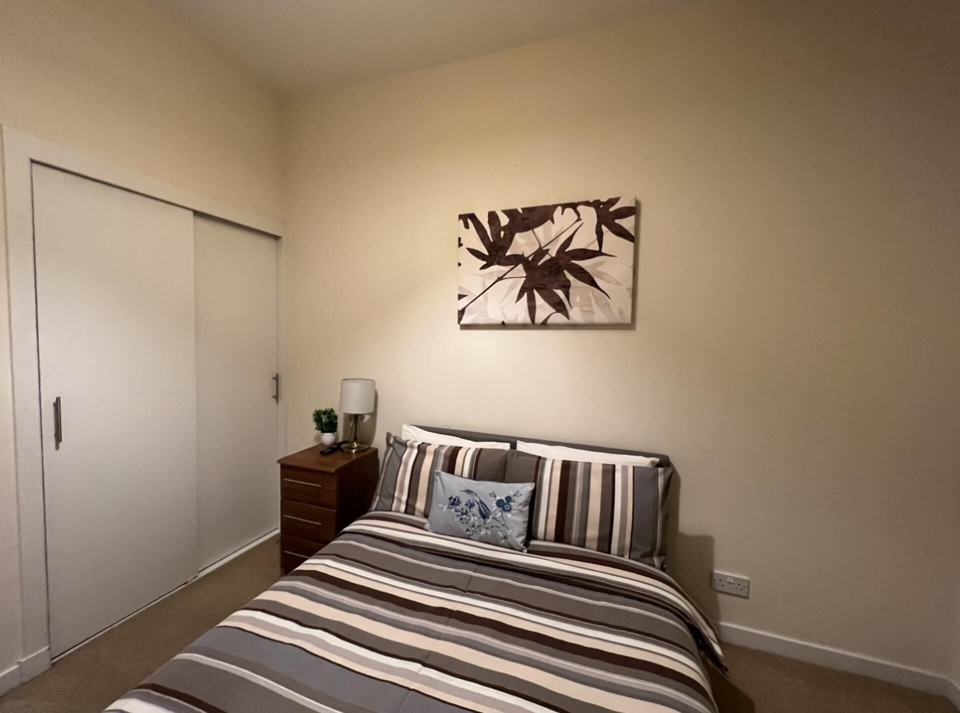 Een slaapkamer met een bed, nachtkastje, wanddecoratie en een gesloten deur.