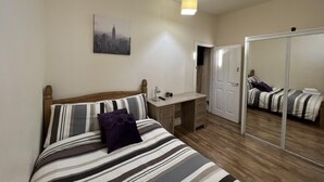 Un dormitorio con cama, escritorio, espejo y puerta.