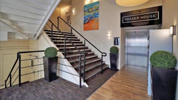 Una escalera que conduce a un ascensor, con un cartel que dice "FRASER HOUSE" encima.