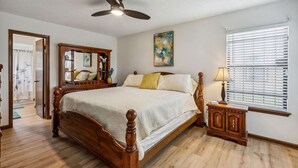 Une chambre à coucher avec un lit en bois, un ventilateur de plafond, une table de chevet avec une lampe et une fenêtre avec des stores.