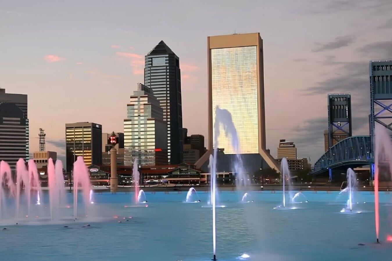A cityscape with modern buildings and a waterfront with fountains.