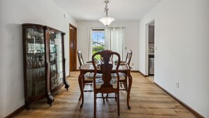 Un coin repas avec une table et des chaises en bois, une vitrine et une vue sur l’extérieur, accessible par une porte.