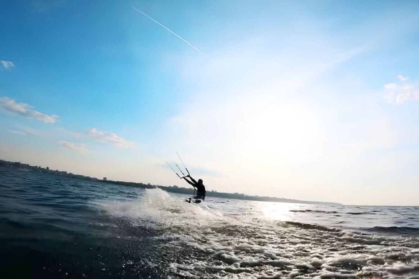A person windsurfing on a body of water with a clear sky in the background.