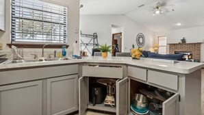 Une cuisine moderne dotée d’un îlot central intégré, d’une fenêtre avec stores et d’un ventilateur de plafond.