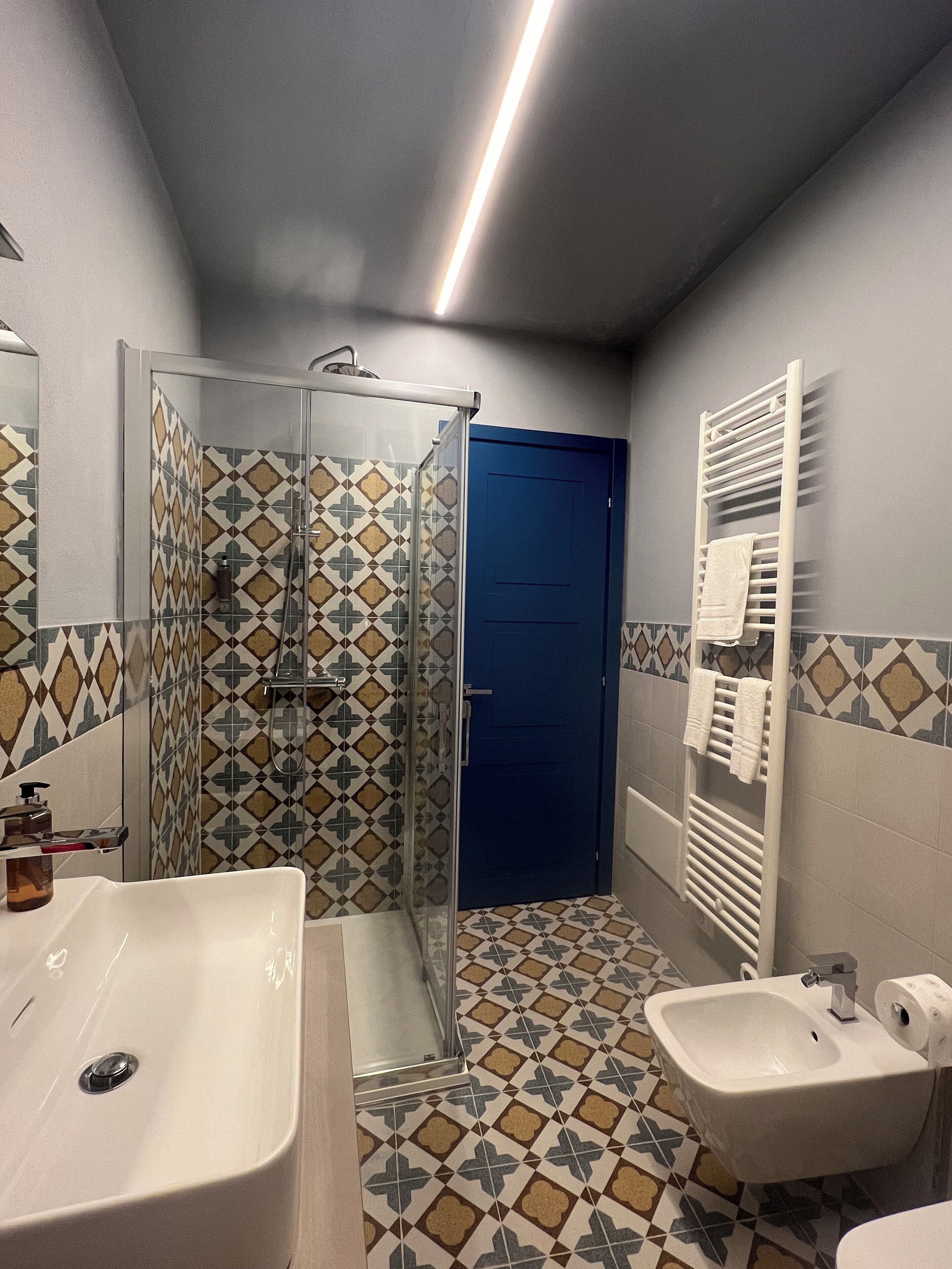 Un baño con cabina de ducha de vidrio, lavamanos, bidé y un perchero para toallas.