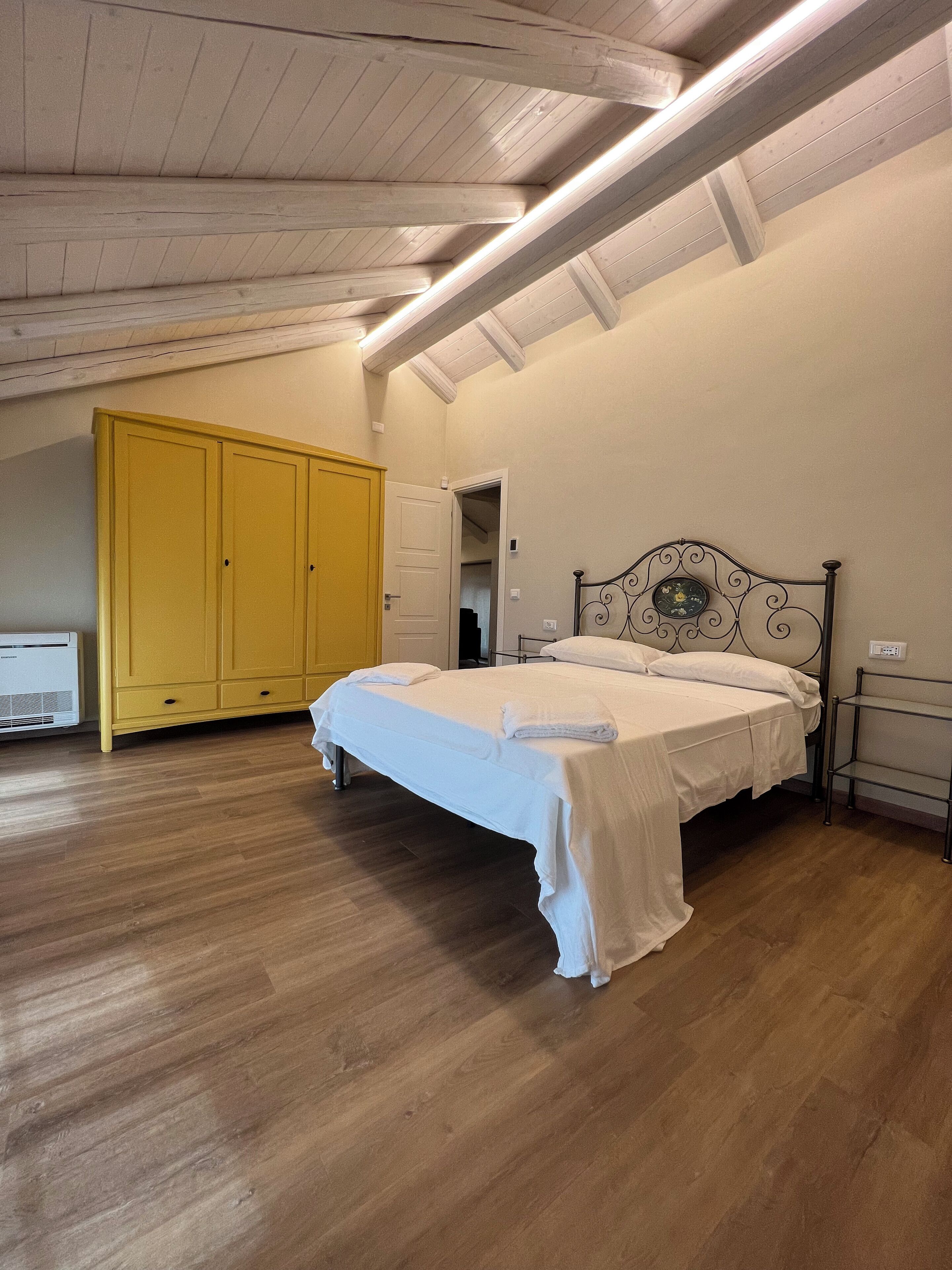 Ein Schlafzimmer mit Bett, Holzboden, einem gelben Kleiderschrank und einer weißen Decke.