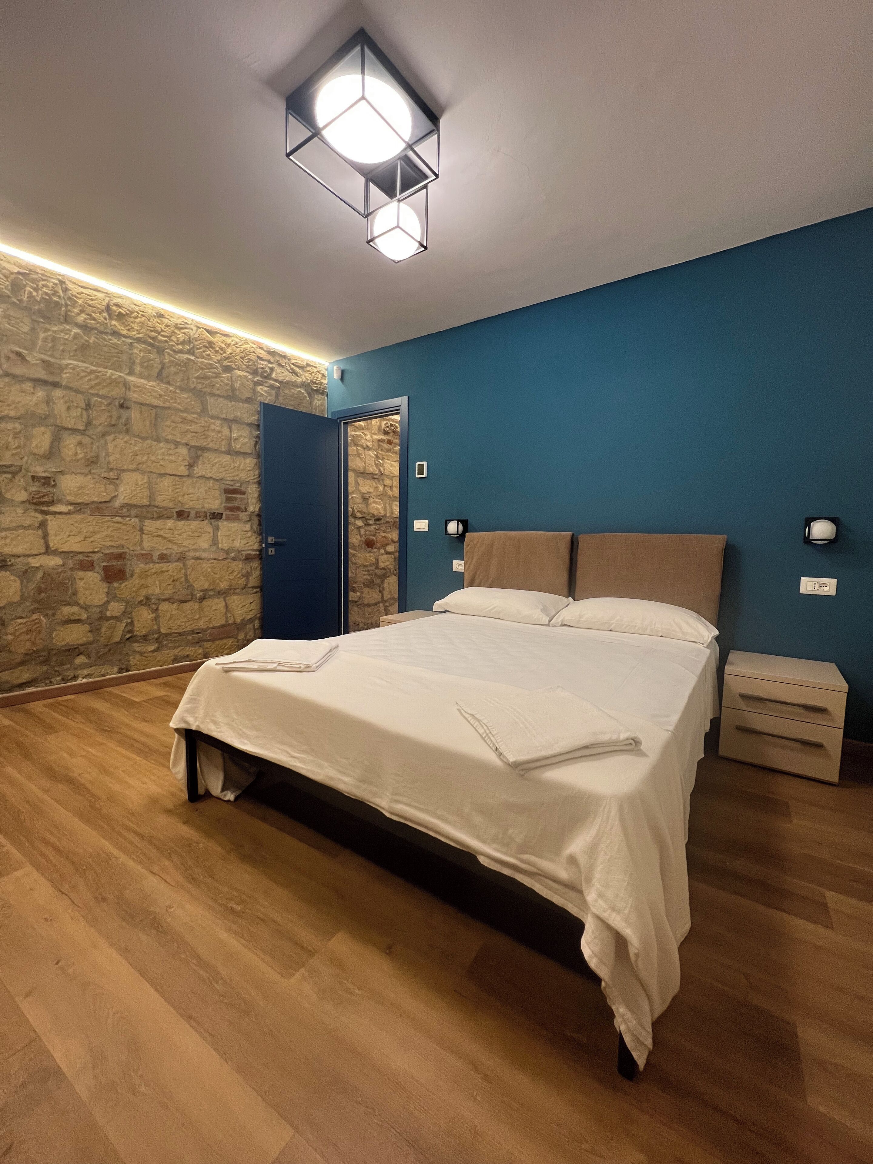 Un dormitorio con una cama, una pared de piedra, una pared azul y suelo de madera.