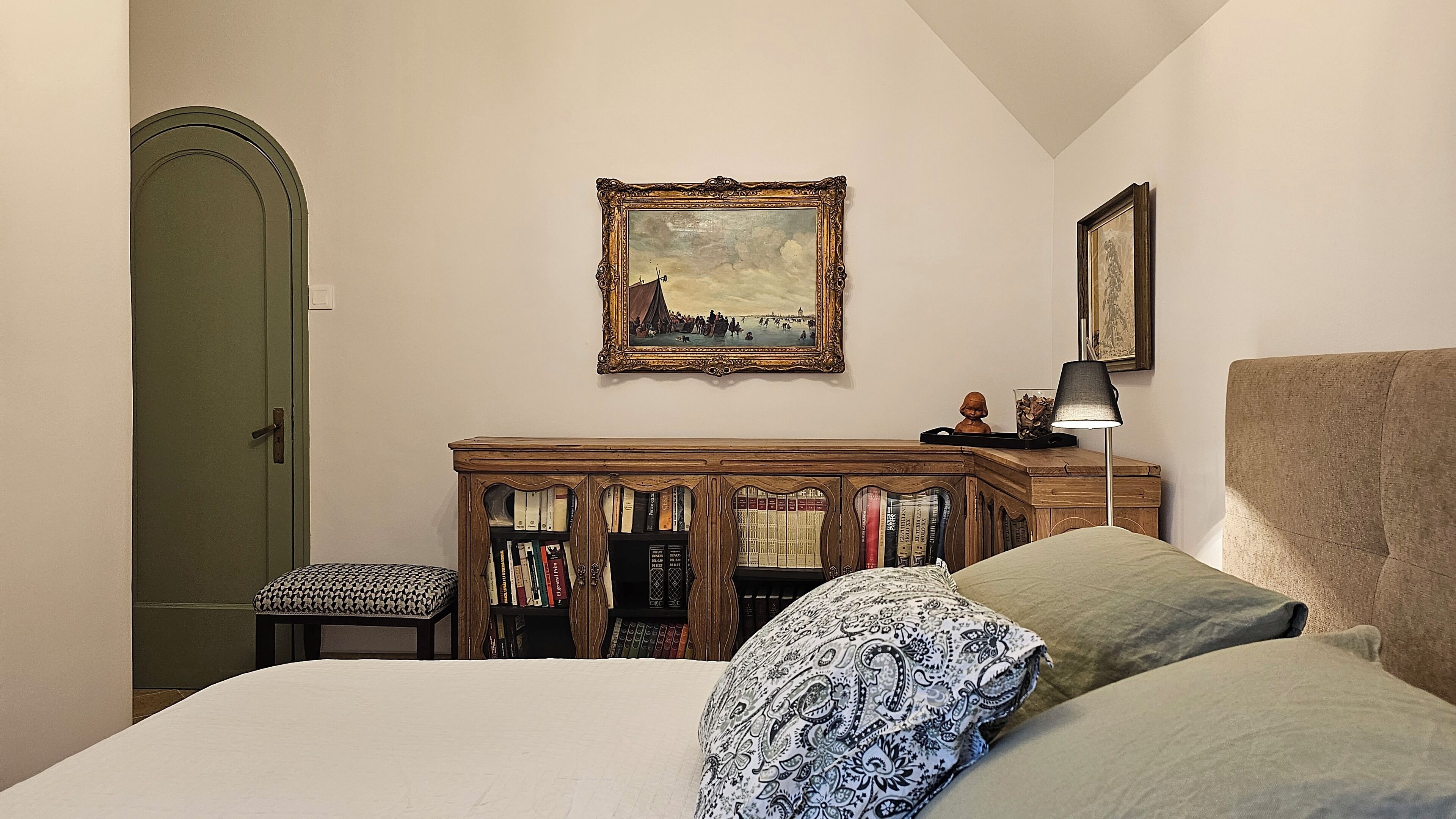 Une chambre à coucher avec un lit, une commode en bois, une bibliothèque et deux tableaux encadrés accrochés au mur.