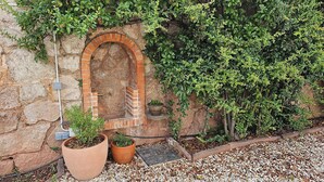 Un muro de piedra con un arco de ladrillo, macetas con plantas y un sendero de grava.